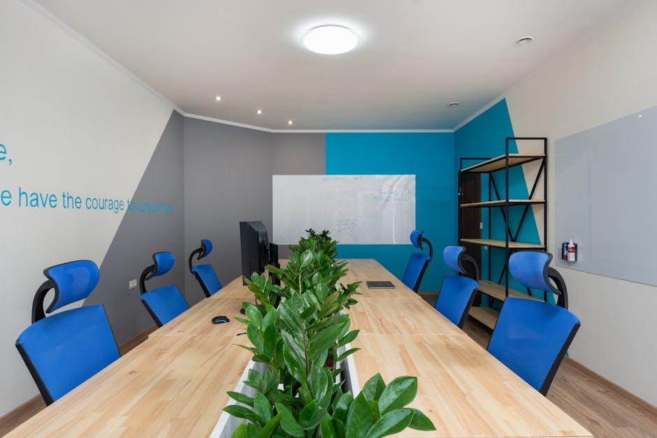 Armchairs at table with green plants placed in light conference room with inscription on wall and shelves in office building